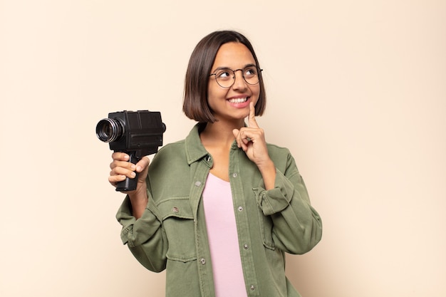 Jeune femme latine souriant joyeusement et rêvant ou doutant, regardant sur le côté