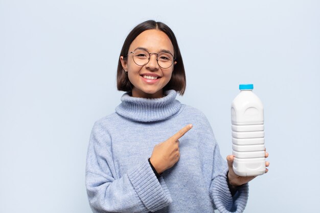 Jeune femme latine souriant joyeusement, se sentant heureuse et pointant vers le côté et vers le haut, montrant l'objet dans l'espace de copie