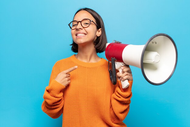 Jeune femme latine souriant joyeusement, se sentant heureux et pointant vers le côté et vers le haut, montrant l'objet dans l'espace de copie