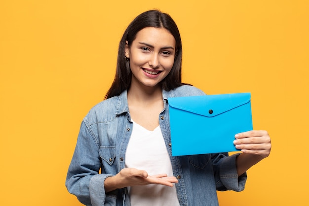 Jeune femme latine souriant joyeusement, se sentir heureux et montrant un concept dans l'espace de copie avec la paume de la main