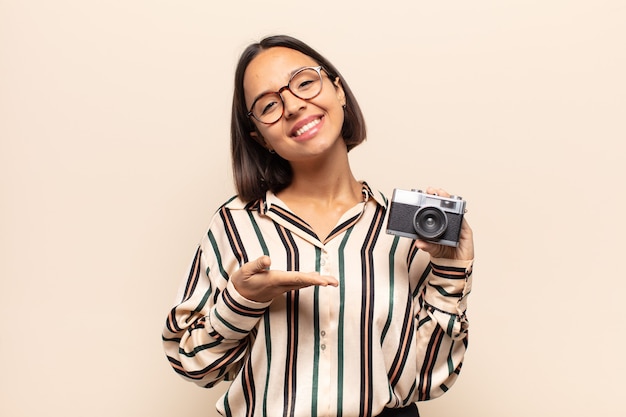 Jeune femme latine souriant joyeusement, se sentir heureux et montrant un concept dans l'espace de copie avec la paume de la main