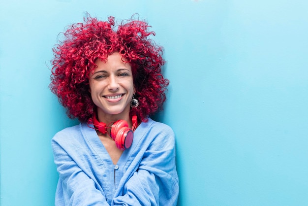 une jeune femme latine souriante avec des cheveux afro rouges sur fond bleu regardant la caméra