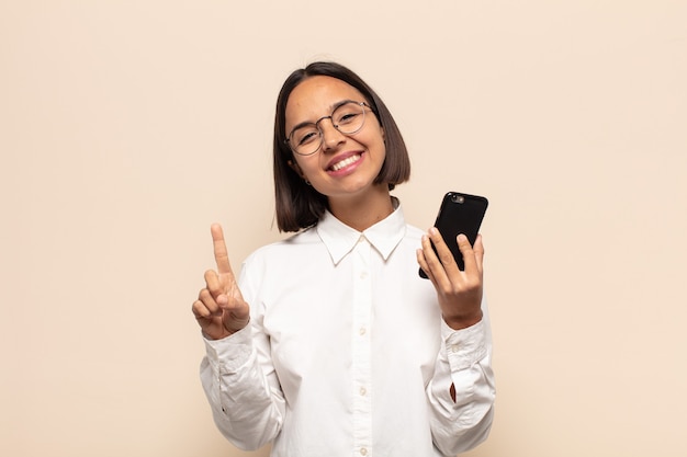 Jeune femme latine souriante fièrement et avec confiance faisant triomphalement la pose numéro un, se sentant comme un leader