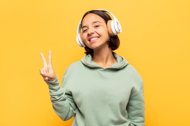 Jeune femme latine souriante et à la recherche heureuse, insouciante et positive, gestes de victoire ou de paix d'une seule main