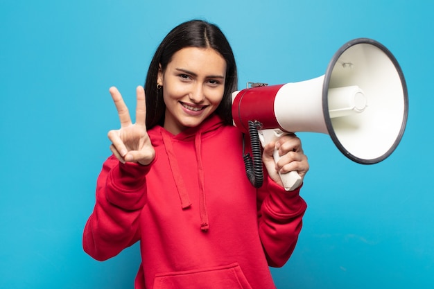 Jeune femme latine souriante et à la recherche heureuse, insouciante et positive, gestes de victoire ou de paix d'une seule main