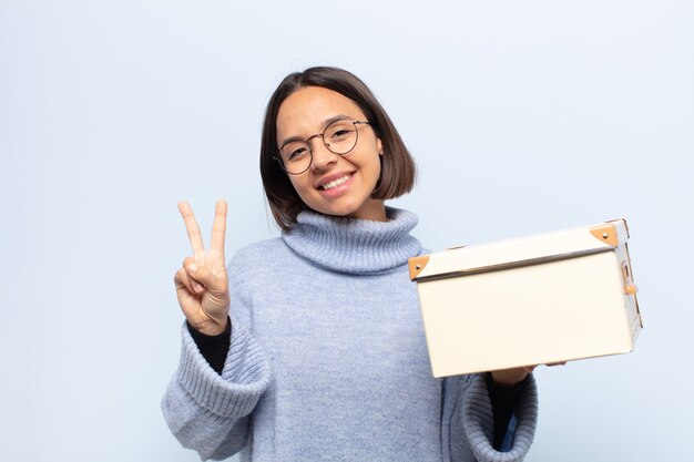 Jeune femme latine souriante et semblant amicale, montrant le numéro deux ou la seconde avec la main vers l'avant, compte à rebours