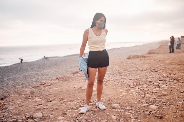 Jeune femme latine sourit pendant un beau coucher de soleil Heureuse jeune femme avec masque sur la plage en prenant