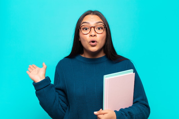 Jeune femme latine à la surprise et choqué, avec la mâchoire tombée tenant un objet avec une main ouverte sur le côté