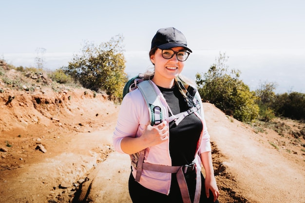 Jeune femme latine de taille plus avec sac à dos, escaladant une colline et faisant de la randonnée dans un magnifique paysage.