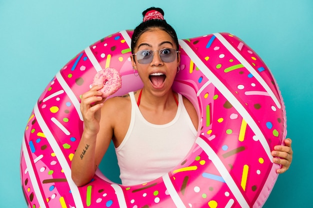 Jeune femme latine tenant un beignet gonflable mangeant un beignet isolé sur fond bleu