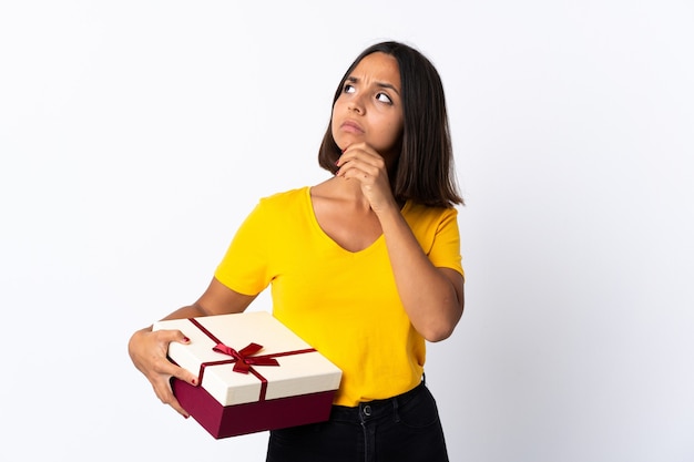 Jeune femme latine tenant un cadeau isolé sur blanc ayant des doutes