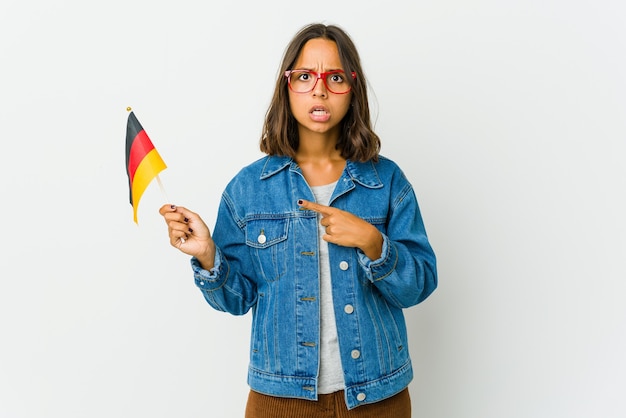 Jeune femme latine tenant un drapeau allemand isolé sur un mur blanc pointant vers le côté