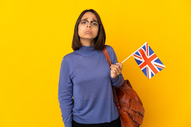 Jeune femme latine tenant un drapeau du Royaume-Uni isolé sur fond jaune avec une expression triste