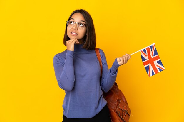 Jeune femme latine tenant un drapeau du Royaume-Uni isolé sur fond jaune en regardant en souriant