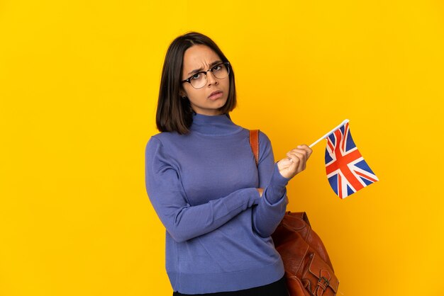 Jeune femme latine tenant un drapeau du Royaume-Uni isolé sur un mur jaune avec une expression malheureuse