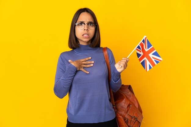 Jeune femme latine tenant un drapeau du Royaume-Uni isolé sur un mur jaune pointant vers soi