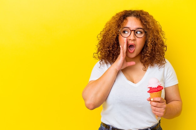 Jeune femme latine tenant une glace isolée sur fond jaune dit une nouvelle secrète de freinage à chaud et regarde de côté