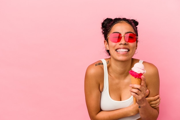 Jeune femme latine tenant une glace isolée sur fond rose en riant et en s'amusant.