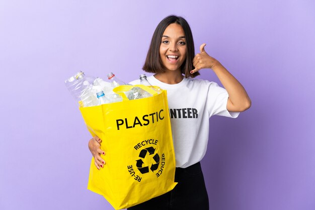 Jeune femme latine tenant un sac de recyclage plein de papier à recycler isolé sur violet