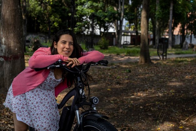 Jeune femme latino-américaine se promène au printemps dans le parc avec son vélo électrique