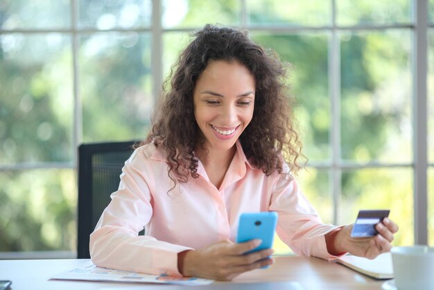 Une jeune femme latino est assise à la maison avec une carte de crédit pour faire des achats en ligne avec un ordinateur.