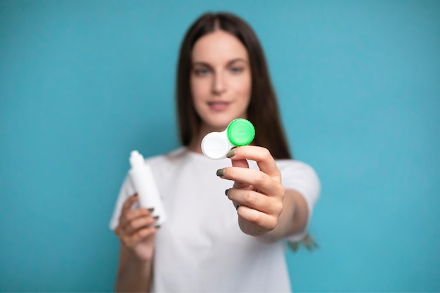 Photo jeune femme avec des lentilles de contact et une bouteille de solution sur un fond de couleur