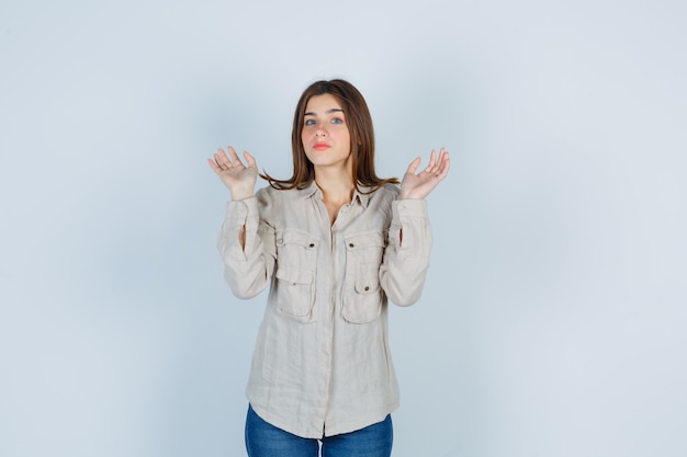 Jeune femme levant les mains en geste d'abandon en jeans décontractés et ayant l'air effrayée. vue de face.