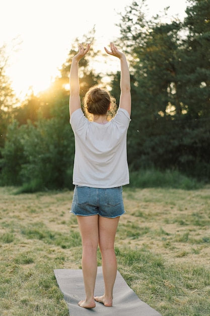 Photo jeune femme levez les mains au soleil dans la prairie au coucher du soleil en plein air relaxant en été