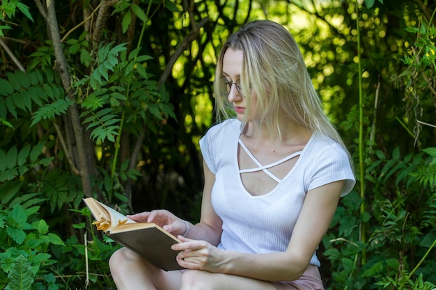 Jeune femme lisant un livre assis dans les buissons au jour d'été, horizontal