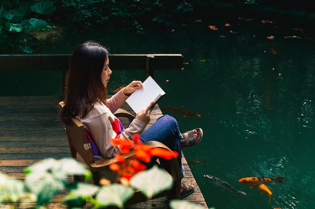 Jeune femme lisant un livre à côté de l'étang.