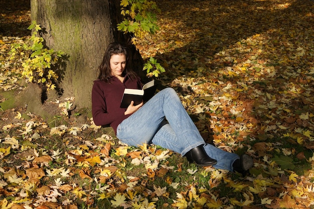 Jeune femme lisant un livre sous un arbre en automne