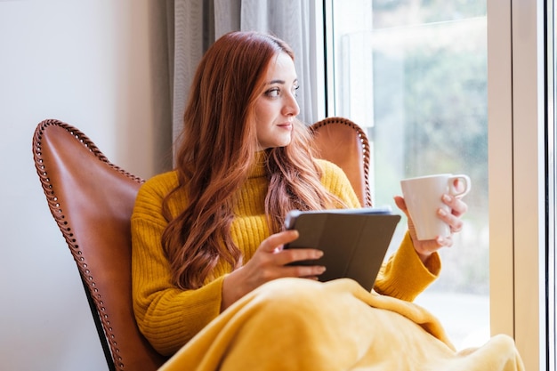 Jeune femme lisant la tablette tout en prenant un café à la maison détendue et reposante