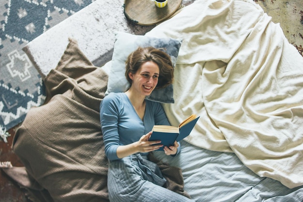 Photo une jeune femme lit un livre allongée sur le lit à la maison.