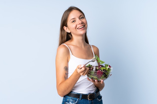 Jeune femme lituanienne sur bleu tenant un bol de salade avec une expression heureuse