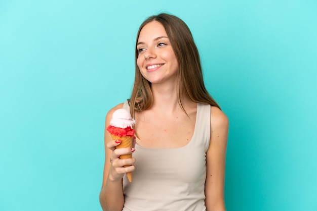 Jeune femme lituanienne avec cornet glace isolé sur fond bleu regardant sur le côté et souriant