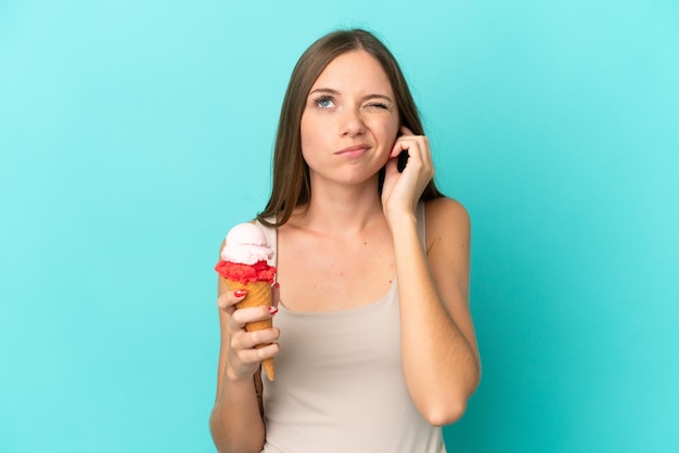 Jeune femme lituanienne avec crème glacée au cornet isolée sur fond bleu frustrée et couvrant les oreilles