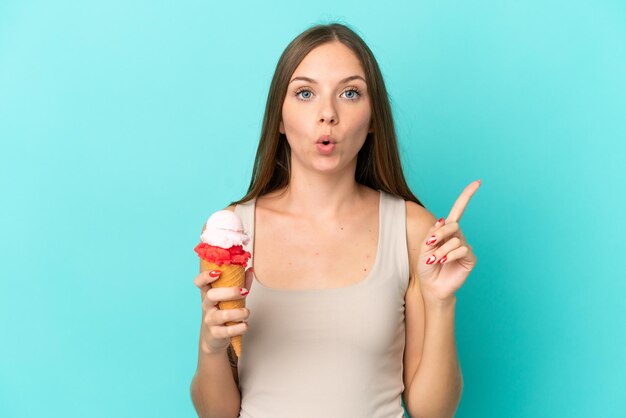 Jeune femme lituanienne avec de la glace au cornet isolée sur fond bleu dans l'intention de réaliser la solution tout en levant un doigt vers le haut