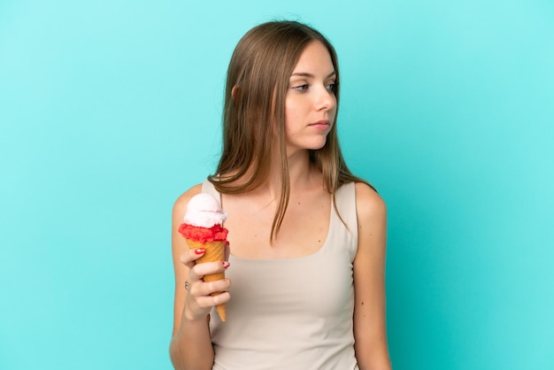 Jeune femme lituanienne avec de la glace au cornet isolée sur fond bleu regardant sur le côté