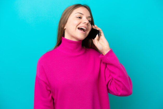 Jeune femme lituanienne isolée sur fond bleu en gardant une conversation avec le téléphone mobile