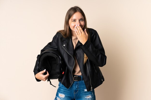 Jeune femme lituanienne tenant un casque de moto sur beige heureux et souriant couvrant la bouche avec la main