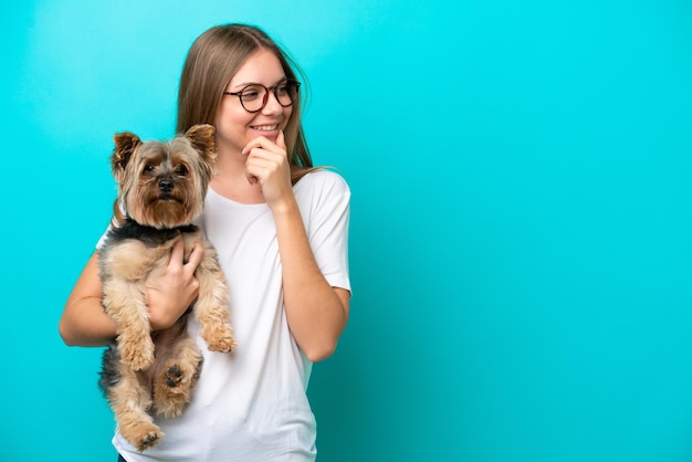 Jeune femme lituanienne tenant un chien isolé sur fond bleu pensant à une idée et regardant de côté