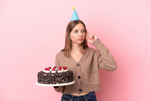 Jeune femme lituanienne tenant un gâteau d'anniversaire isolé sur fond rose ayant des doutes et pensant