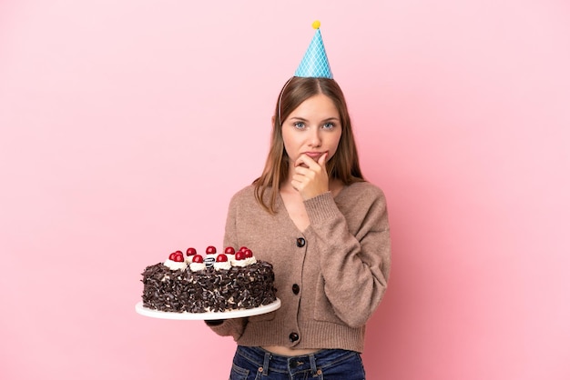 Jeune femme lituanienne tenant un gâteau d'anniversaire isolé sur fond rose pensant