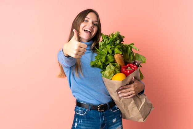 Jeune femme lituanienne tenant un sac d'épicerie avec les pouces vers le haut parce que quelque chose de bien s'est passé