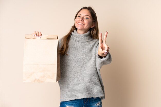 Jeune femme lituanienne tenant un sac d'épicerie souriant et montrant le signe de la victoire