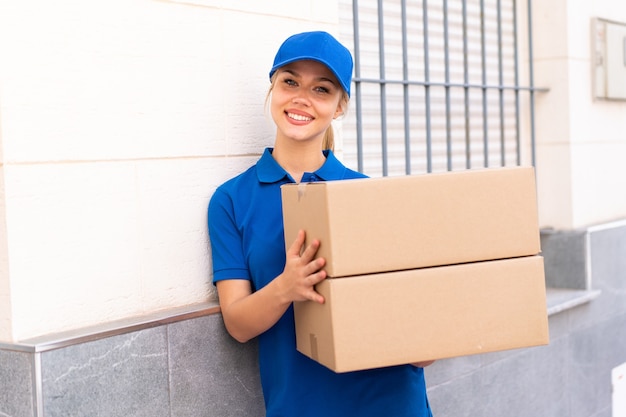 Jeune femme de livraison à l'extérieur tenant des boîtes avec une expression heureuse