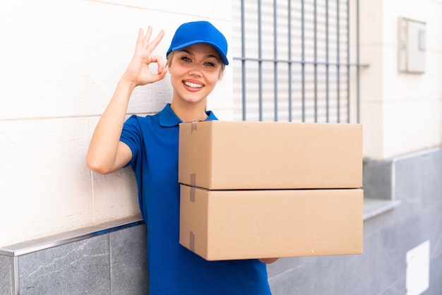 Jeune femme de livraison à l'extérieur tenant des boîtes avec une expression heureuse