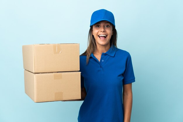 Jeune femme de livraison isolée sur fond bleu avec une expression faciale surprise