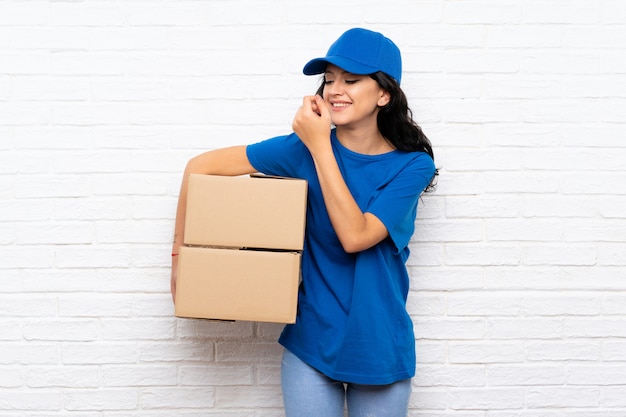 Jeune femme de livraison sur mur de briques blanches souriant beaucoup