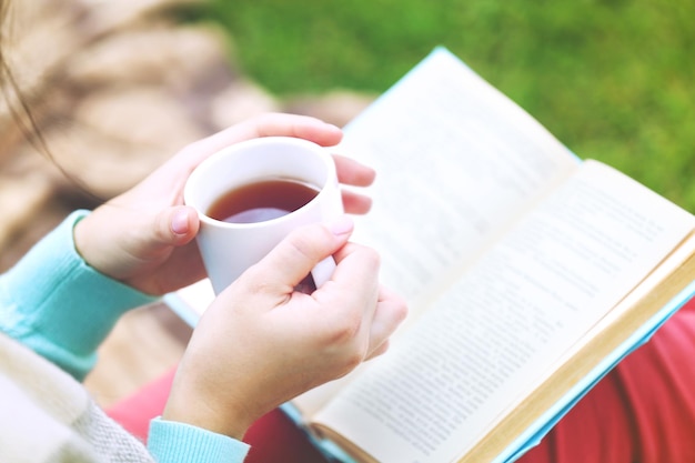 Jeune femme avec livre assis sur l'herbe verte à l'extérieur